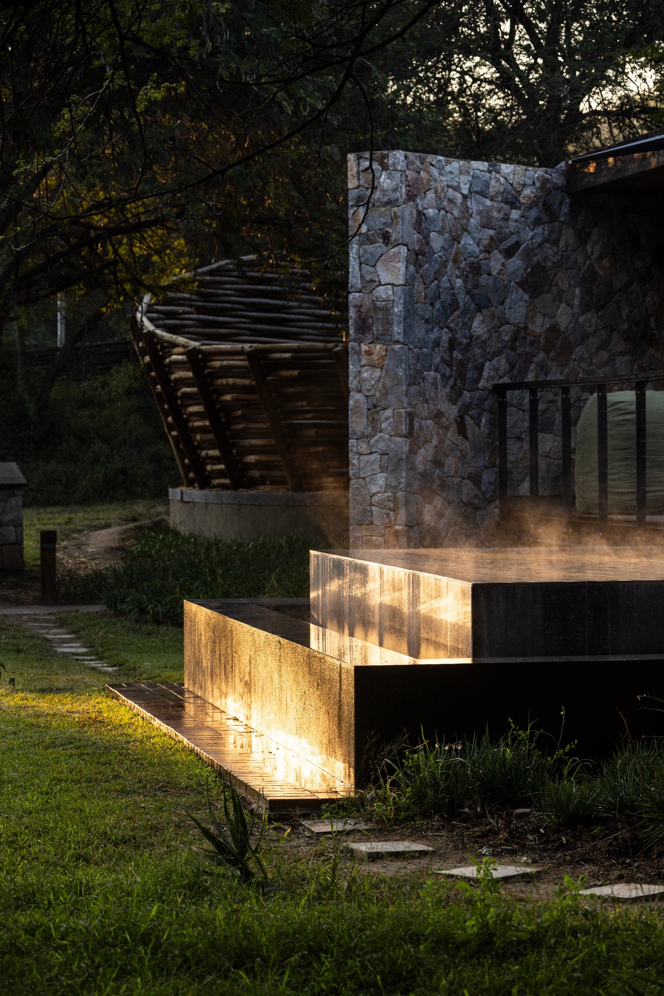 Sunlit water feature beside stone walls and timber architecture at Tanda Tula